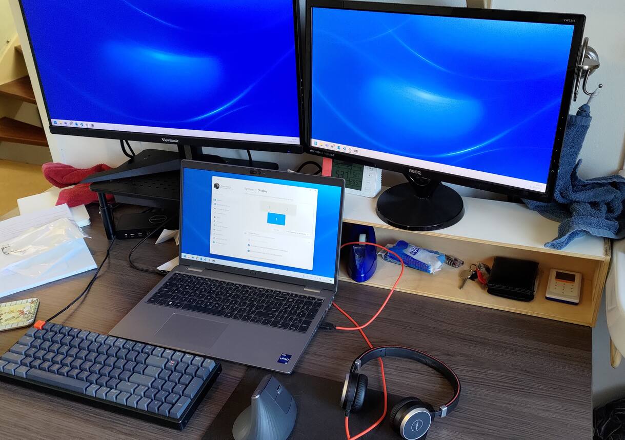 Photo of two monitors connected to a laptop.
There's a wireless mouse and a keyboard with a wire that goes to a box underneath the left monitor.
The laptop has a wire going to this same box.